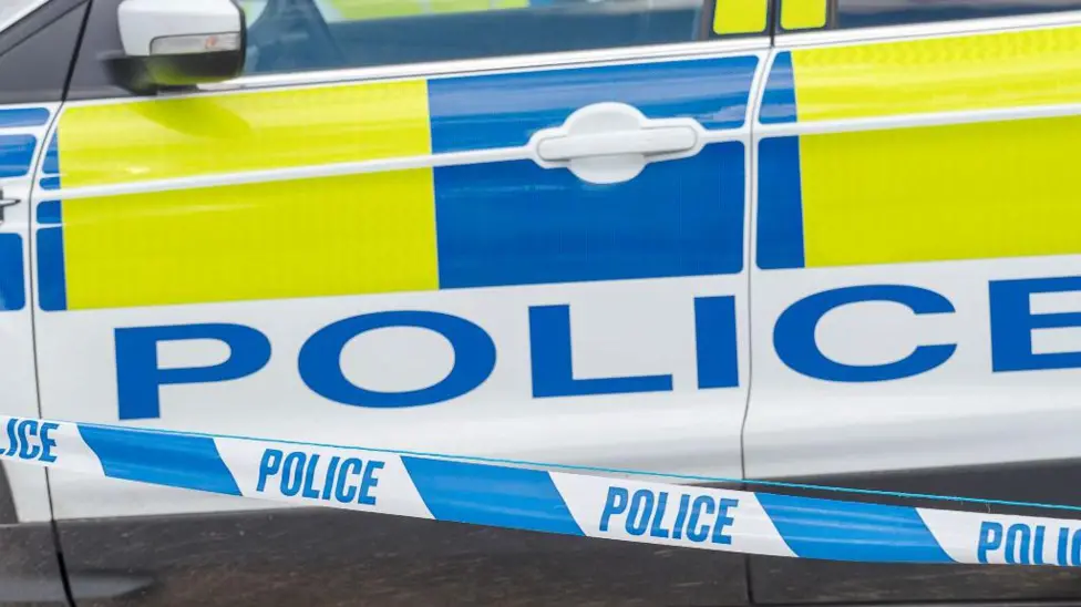 A close-up stock image of the side of a police car with blue and white police tape in front of it.