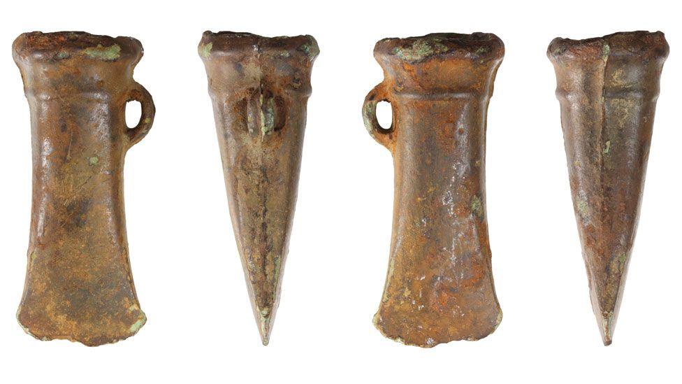 Four views of a bronze socketed axe head with double mouldings at the socket and a side loop. The cutting edge is slightly flared. The views all show the socket edge at the top and the cutting edge at the bottom. They show from left to right, the flat edge with the intact loop on the right; a side view with the loop on top; the flat edge with the intact loop on the left; a side view without the loop.