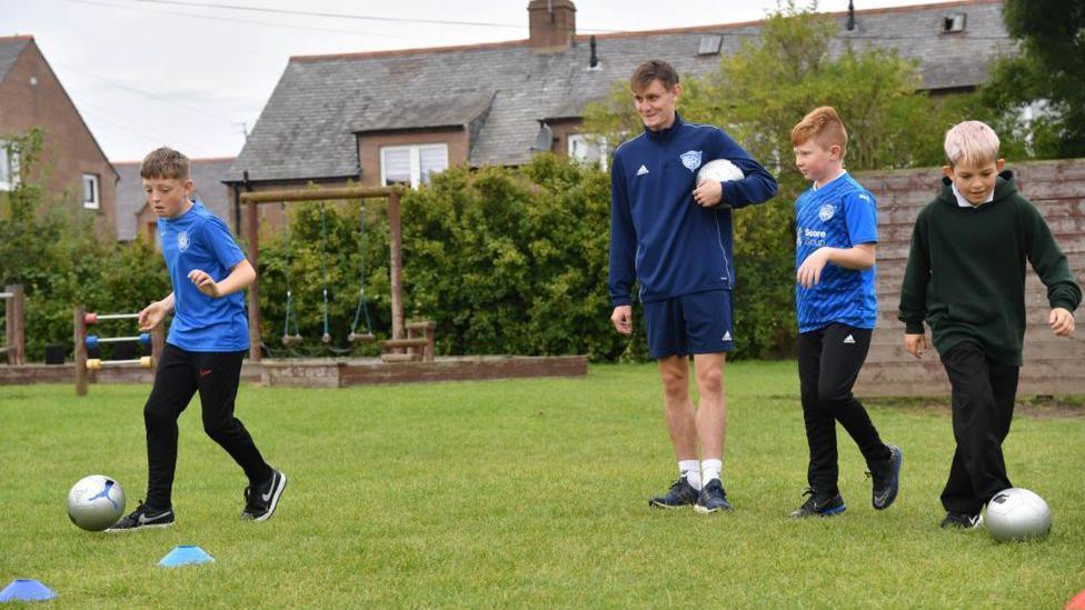 Pupils and coach dribbling footballs.