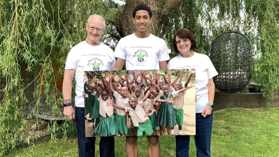 England star Jude Bellingham stood with Rita and Geoff holding an enlarged photograph of children at the school