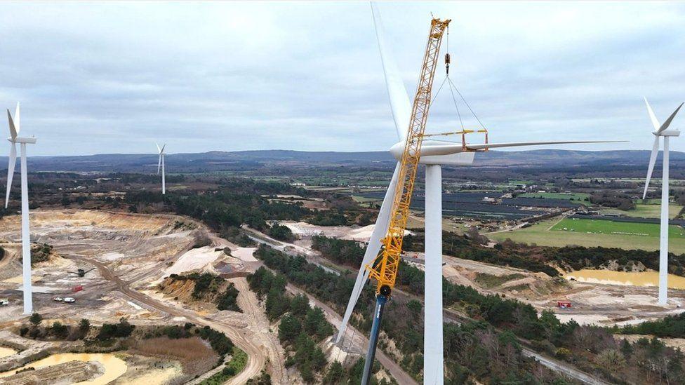 Four white wind turbines set within series of tree-lined pits 