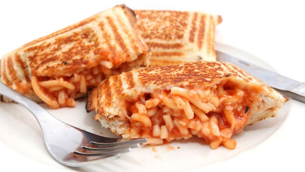Three toasties made with spaghetti in tomato sauce are on a white plate, with some of the spaghetti oozing out of them