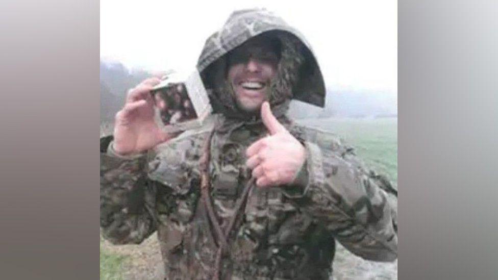 Anthony Rogers wearing a camouflage jacket, doing a thumbs up.