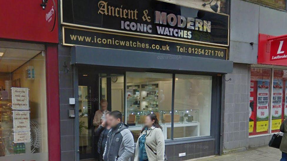 Street view image of Ancient and Modern Jewellers. A glass fronted shop with jewellery cases on display, and black and gold signage. People are walking past
