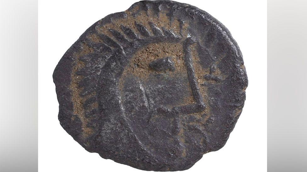 A close up of a silver Iron Age coin showing the face of a man in profile with hair sticking up in spikes