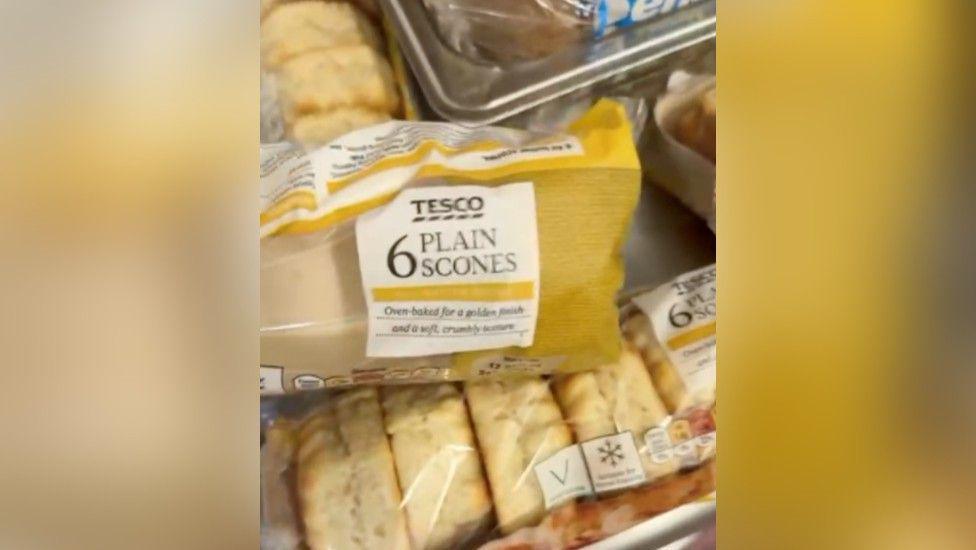 A close-up of several packages of Tesco's '6 plain scones' on a counter. The corner of a gluten-free loaf of bread can be seen in the top right corner.