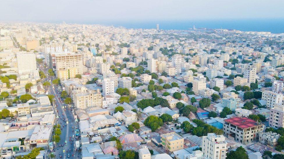 A view from up high of Mogadishu showing a main road and lots of new multi-storey buildings and the sea seen on the horizon