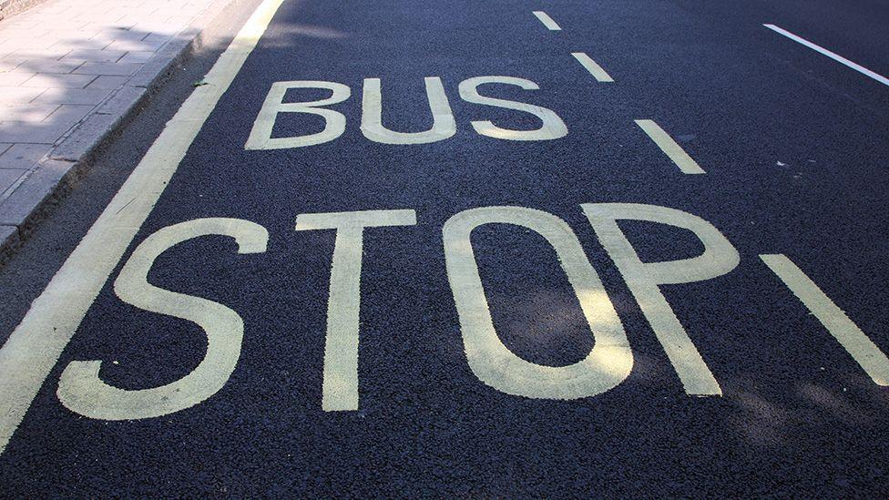 A sign painted on an asphalt road saying 'bus stop' in yellow