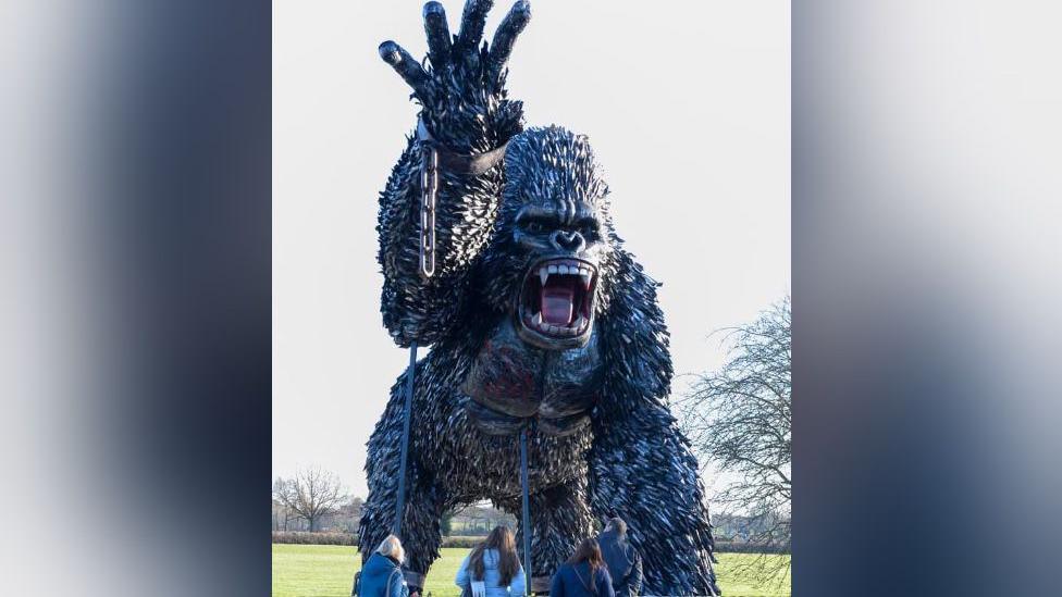 A giant gorilla sculpture made of iron roaring with one arm in the air with a broken metal handcuff around its wrist