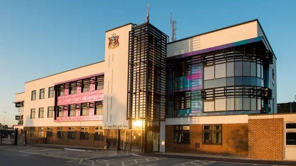 Thames Valley Police headquarters. The top floors have modern-looking cladding in colours of grey and pink and blue, and large glass windows, and it has a red brick ground floor. 