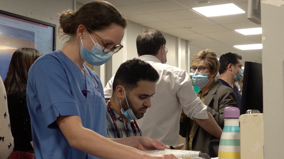 A busy A&E with staff working, wearing face masks, outside the main ward.