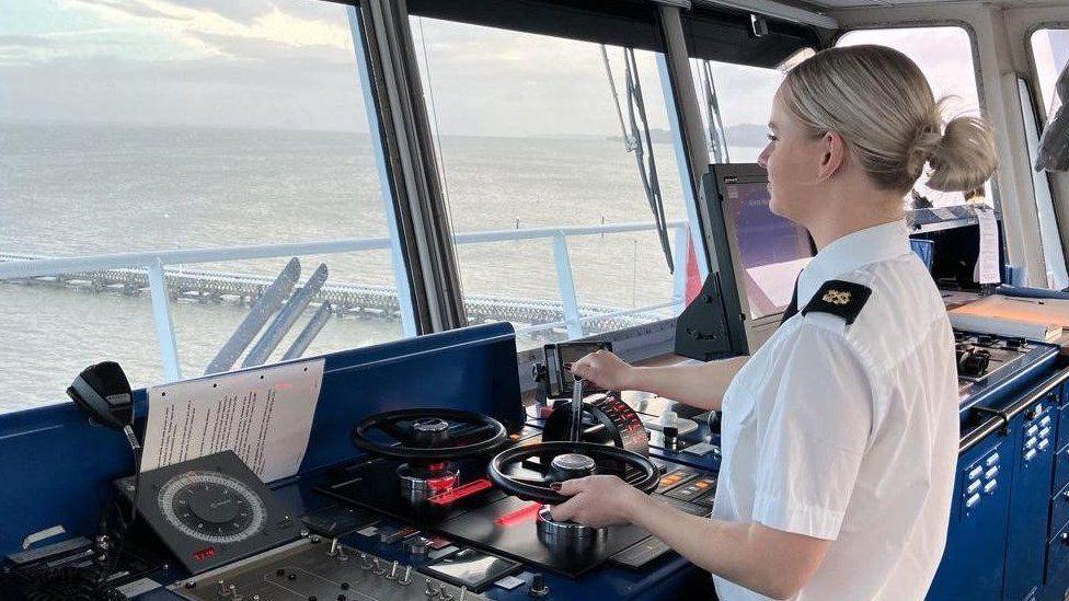 Lauren Lucas helming Wight Sky car ferry. She is in uniform with a white shirt and black epaulettes. She has her back to the camera and is looking out towards the Solent.