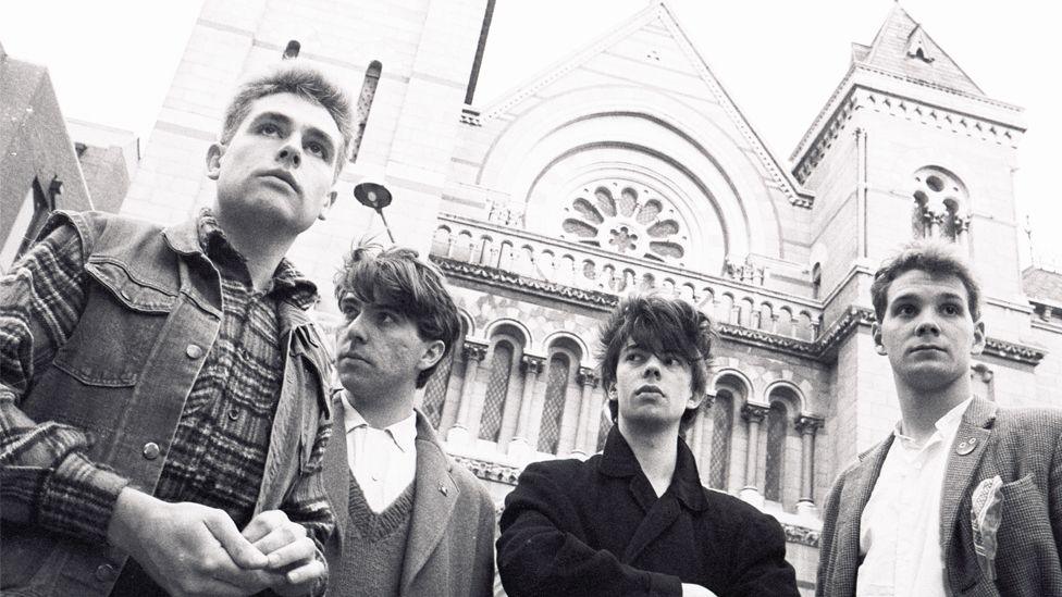 A black and white image of Echo & the Bunnymen in the 80s all looking away from the camera in front of a cathedral