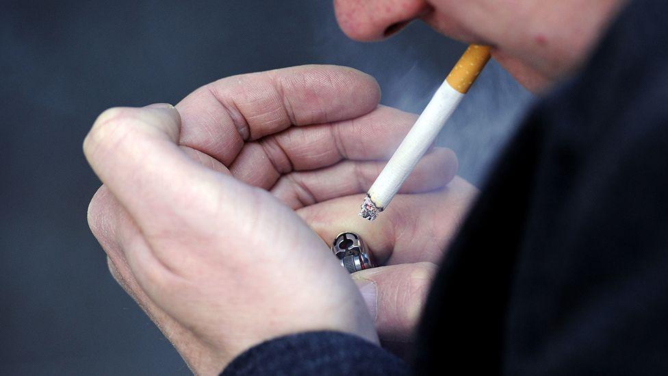 A man with his hands cupped lighting a cigarette with a lighter