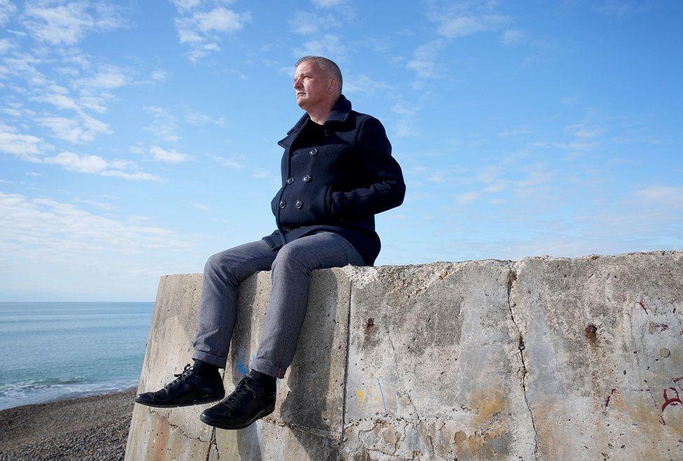 Craig Jones sat on a stone walls looking out to sea on a beach