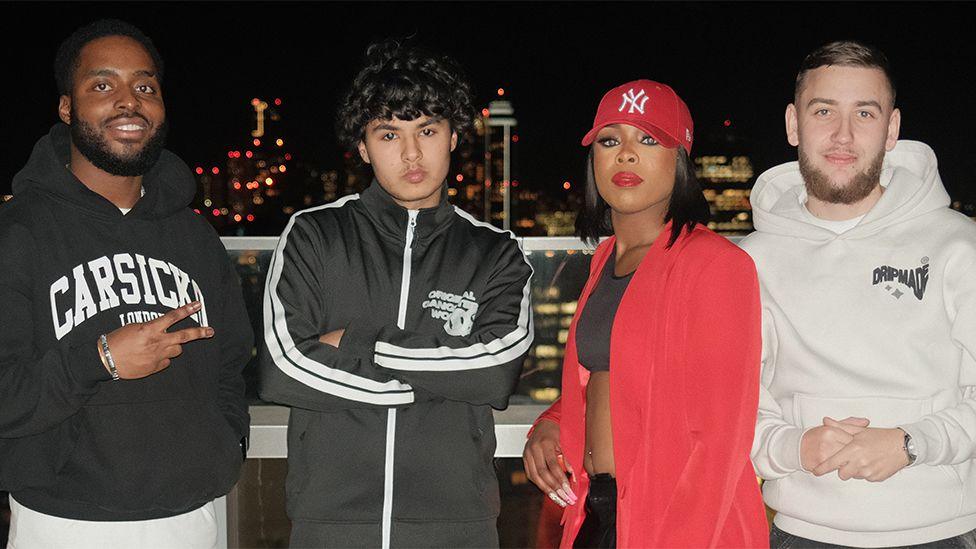 Finalists Only Zizou, Haydog, Layyah, CBliminal standing at the top of a London skyscraper, with the lights of big buildings behind. Cbliminal is  wearing a cream hoodie. Haydog has got curly hair - wearing a black zip up jacket and grey jeans. Layyah - wearing a black top, red blazer and red hat. Only Zizou is smiling with his hands clasped wearing a black hoodie and ripped jeans. 