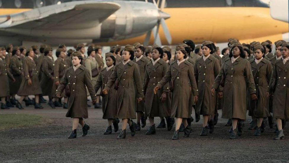 A still from the film. It shows a row of women in US World War Two uniform marching past two aeroplanes