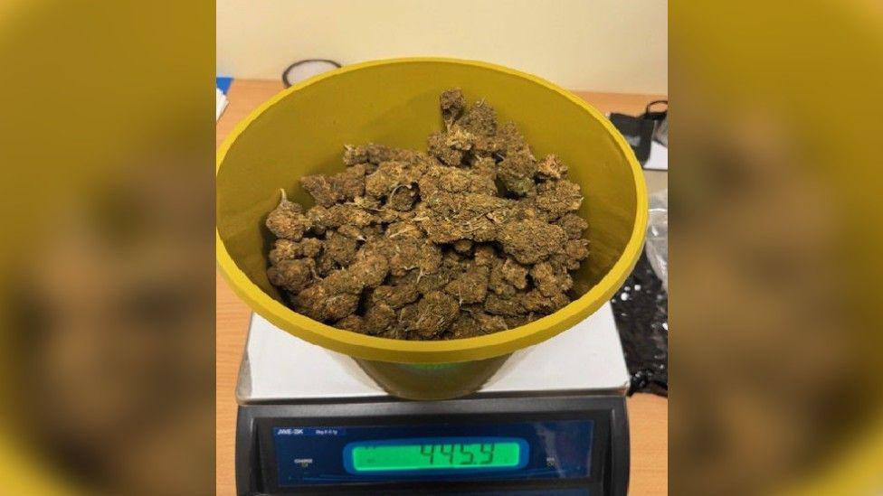 A deep yellow bowl on a set of scales filled with cannabis. The scales say 445.9