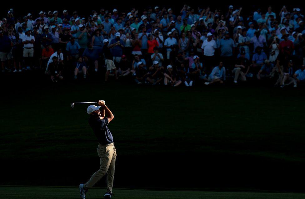 Scottie Scheffler plays a shot on the 18th hole during his final round of the US PGA Championship with the crowd mostly cast in shadow. Photo by Andrew Redington