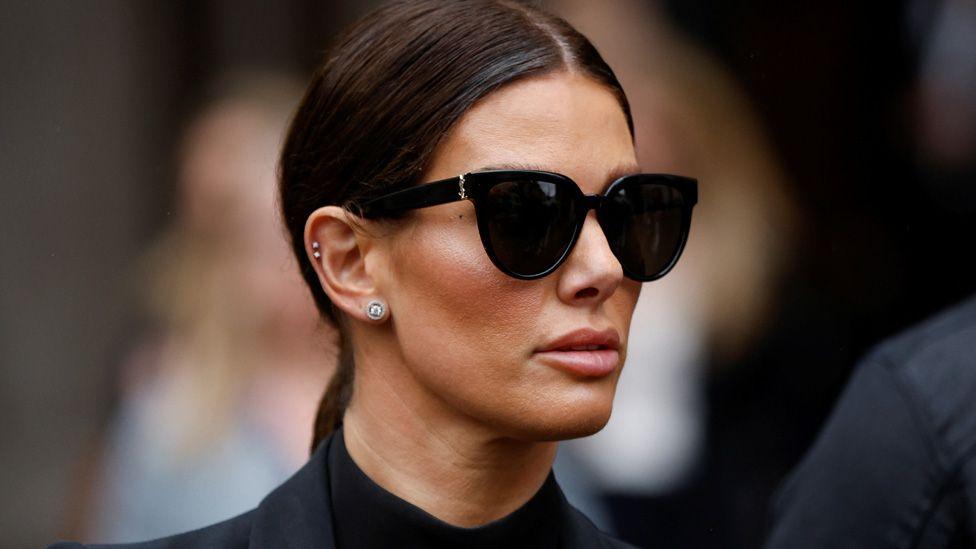 Rebekah Vardy in dark glasses and a dark suit outide court in 2022