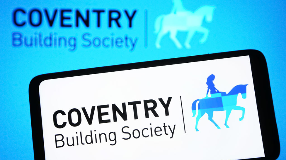 Coventry Building Society logo on a smartphone, with the firm's sign in the background