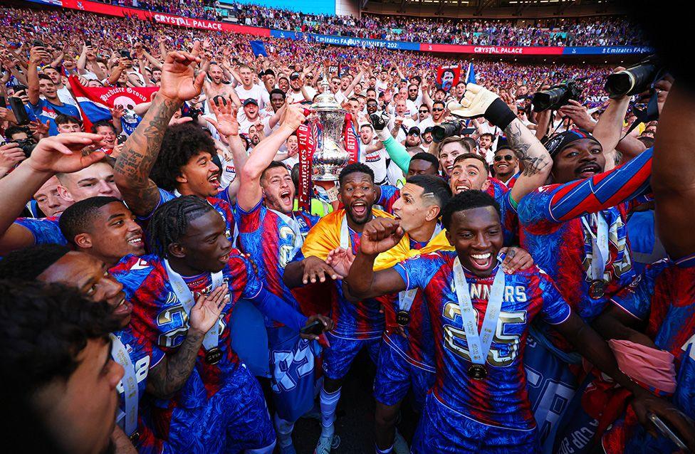 Crystal Palace's Joel Ward lifts the FA Cup trophy at Wembley, surrounded by team-mates and fans. Photo by Marc Atkins