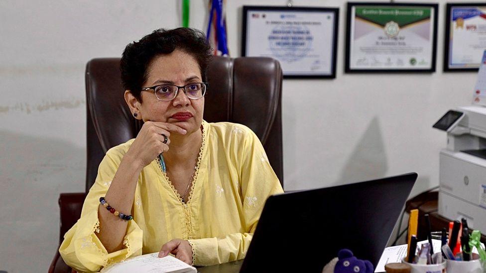 Dr Syed sitting at her desk wearing a yellow top