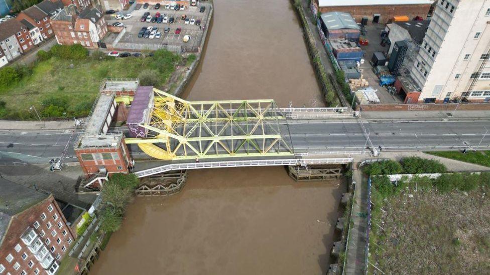 Aerial view of Drypool Bridge which has a yellow metal lifting mechanism and brick control room at one end spanning the roadway