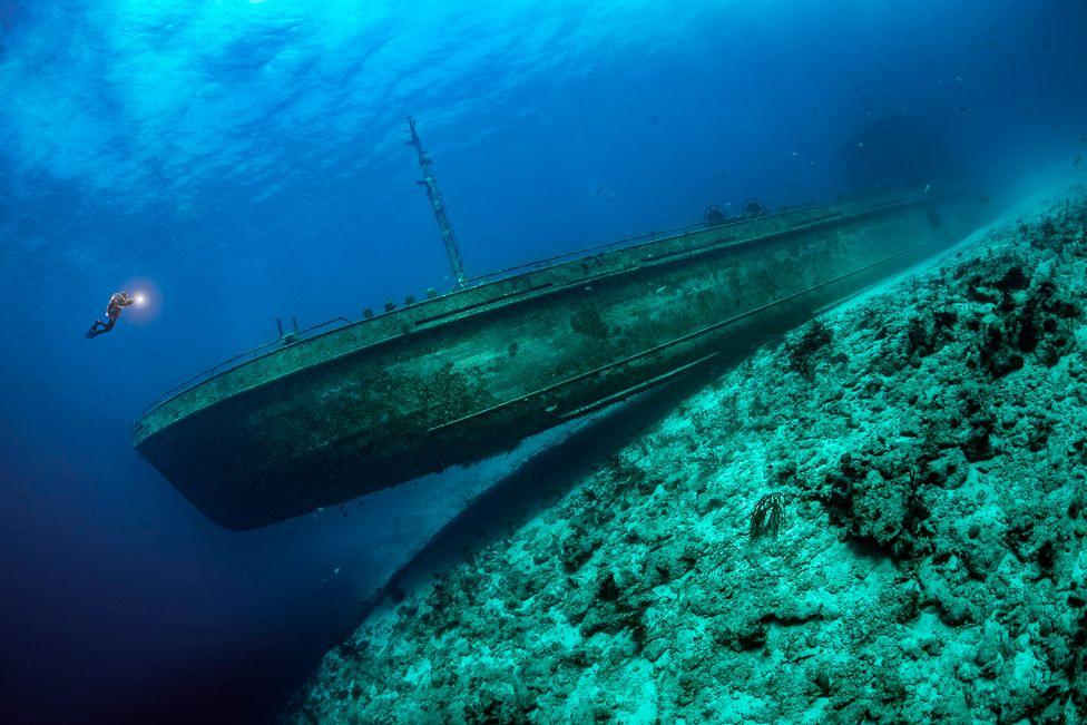 A scuba diver is dwarfed by a shipwreck in the Bahamas
