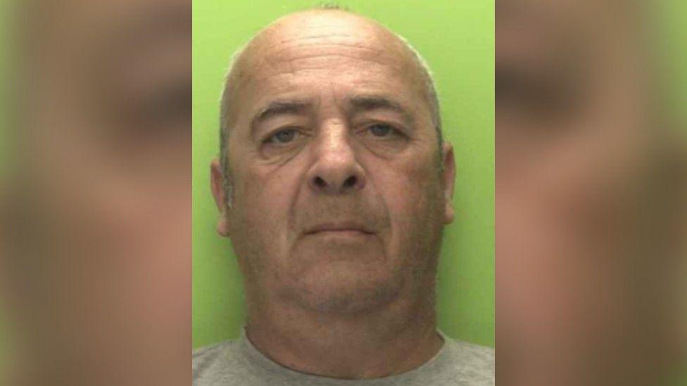 A police custody shot of a middle-aged bald man in a get t-shirt