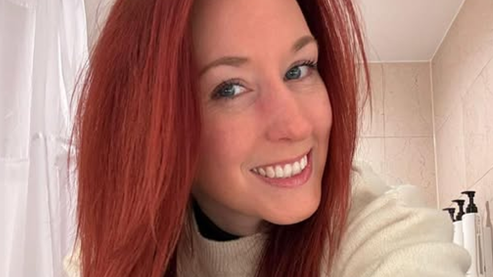 Sian Haddon has long, dyed red hair. She smiles for the camera.