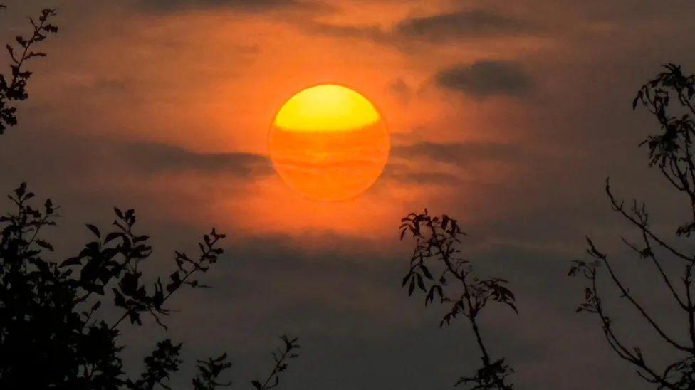 A summer moon is seen in the sky. It is orange with a yellow top