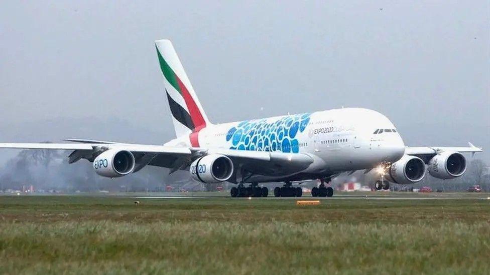 An Emirates airline plane at Glasgow Airport. It is predominantly white with a blue design on the body and red, green and black flag on the tail.