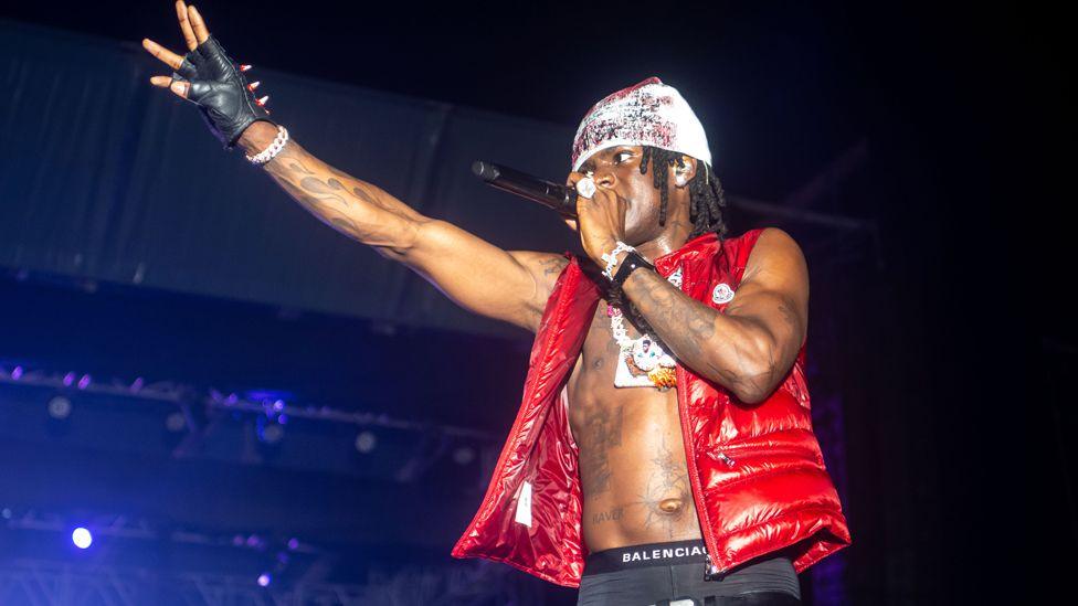 Nigerian singer wearing a red puffer gilet over his bare torso on which he has many tattoos performs at a concert at Eko Energy City Gate, Lagos - 22 December 2024