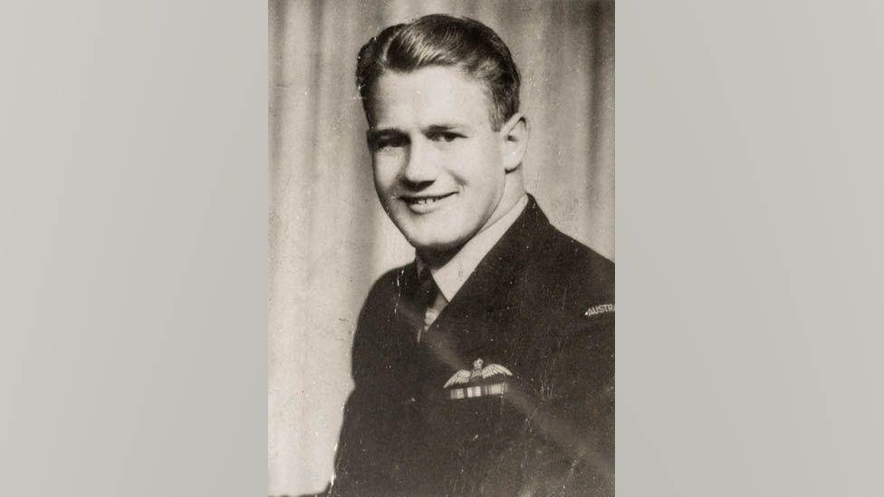 A black and white photograph of Neville Emery wearing the uniform of the Royal Australian Air Force. He is turned slightly to face the camera and is smiling. His hair is slicked back.