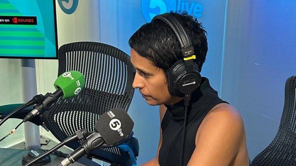 Naga Munchetty wearing headphones talking into 5Live microphone in a studio