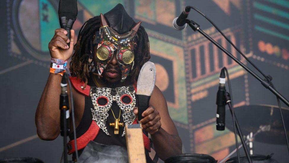 A member of the Democratic Republic of Congo band Fulu Miziki wearing a mask prepares the stage for his bands performance