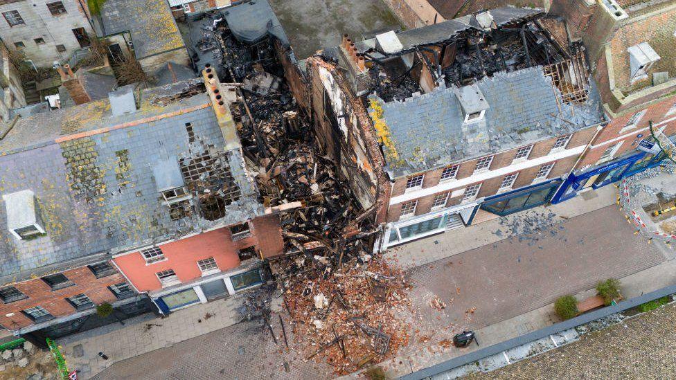 Gaping holes in roofs of terrace after fire - rubble from building in centre spills onto street.