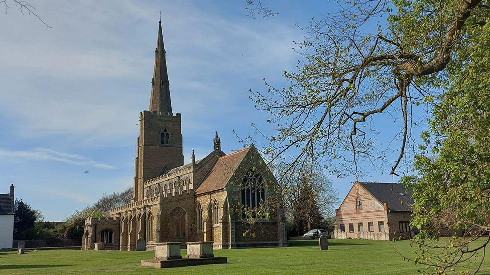 St Wendreda's Church in March - it has a tall spire. The churchyard has a few headstones on an otherwise open grassy expanse.