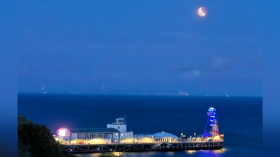 A lit up pier sits below a bright moon.