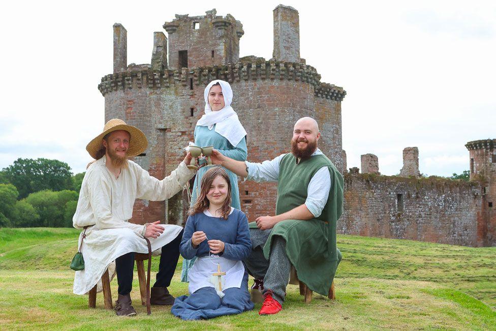 A group of people dressed up in medieval costume stand in front of a crumbling castle
