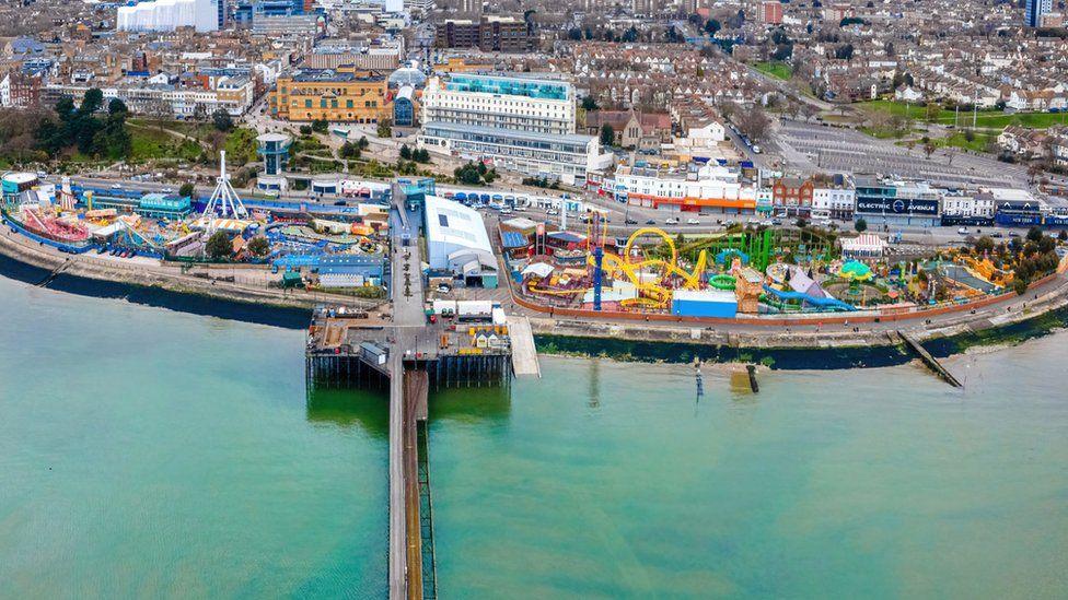 A drone picture of Southend's pier and the Adventure Island theme park. The sea is a mix of greens and blues. Houses and large city buildings are in the background.