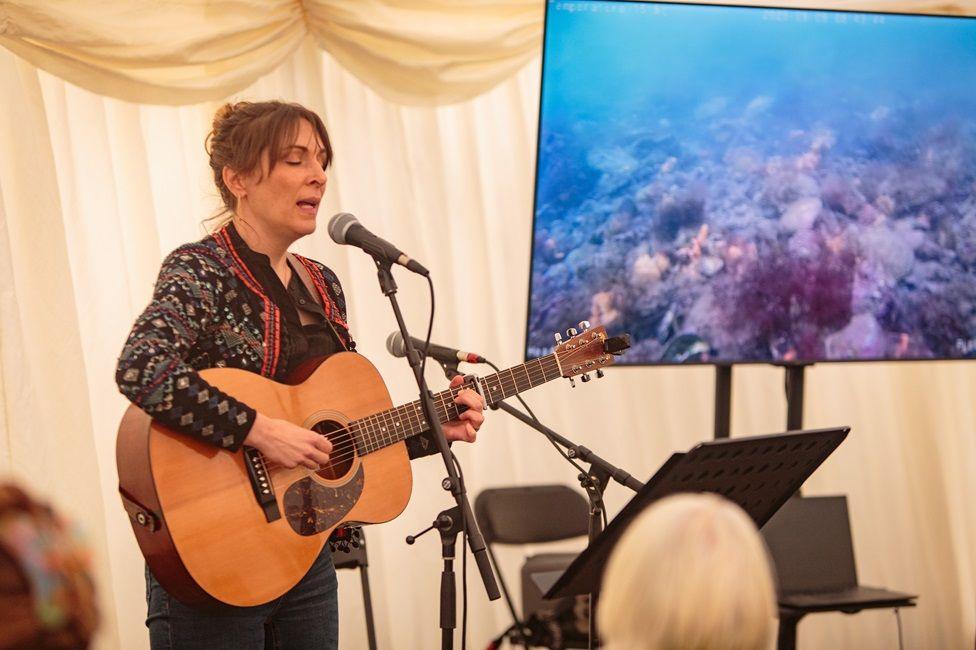 Folk singer Emily Smith with her eyes closed plays the guitar and sings into a microphone