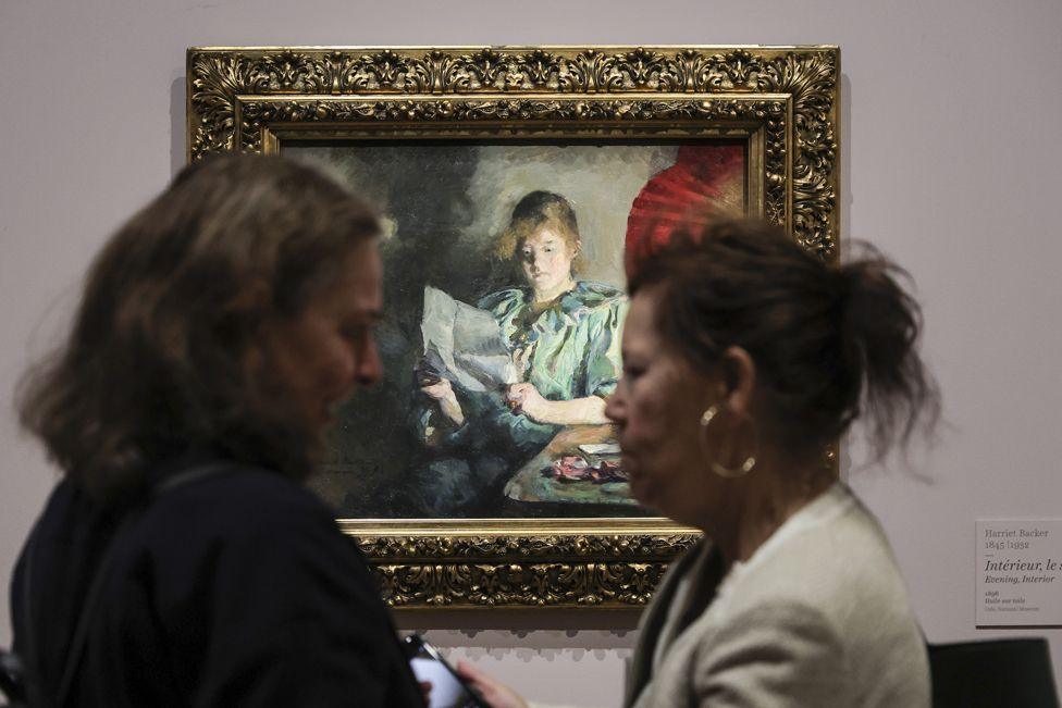 Two women talking in front of the painting 'Evening. Interior' by Harriet Backer during the press tour of the exhibition 'Harriet Backer. The music of colours' at Orsay Museum in Paris, France, 20 September 2024. 