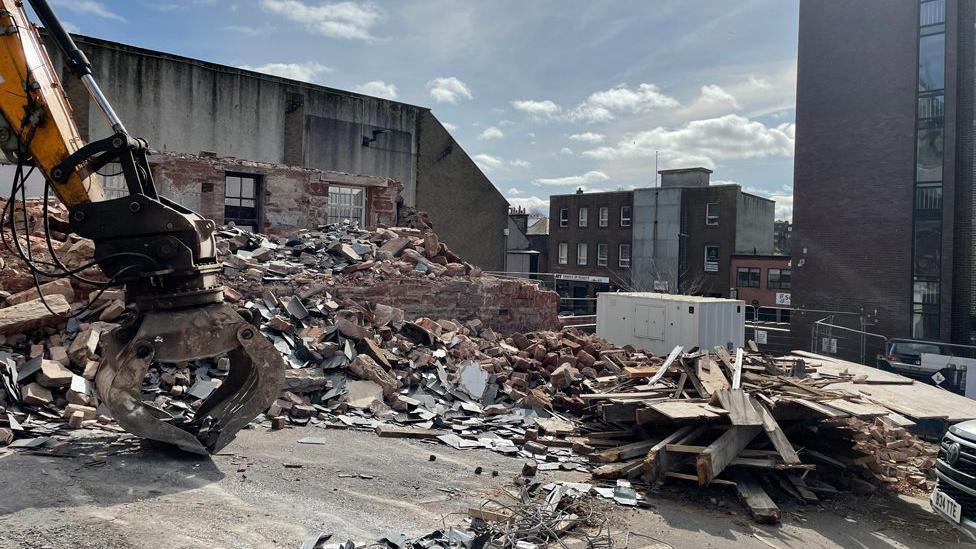 A pile of rubble and industrial machinery on a building site with some tall buildings in the background