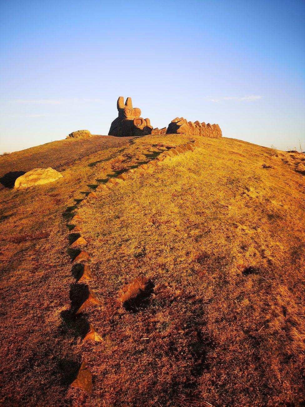 A dragon statue on the top of a hill cuts a clear figure in the last sunlight of a cold but clear winter day