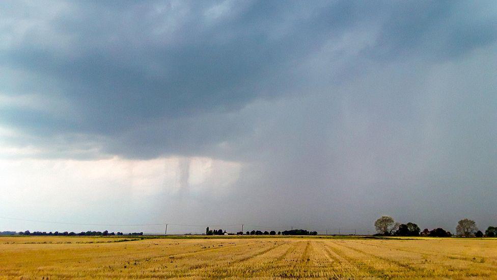 Dark clouds and rain roll in over harvested wheat fields in the flat Cambridgeshire Fens