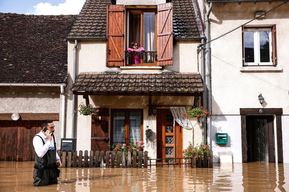 A woman watches from her balcony as a local police officer wades through the flood waters in front of her house in Tresmes, Seine-et-Marne department, Ile-de-France region, France, 10 October 2024.  