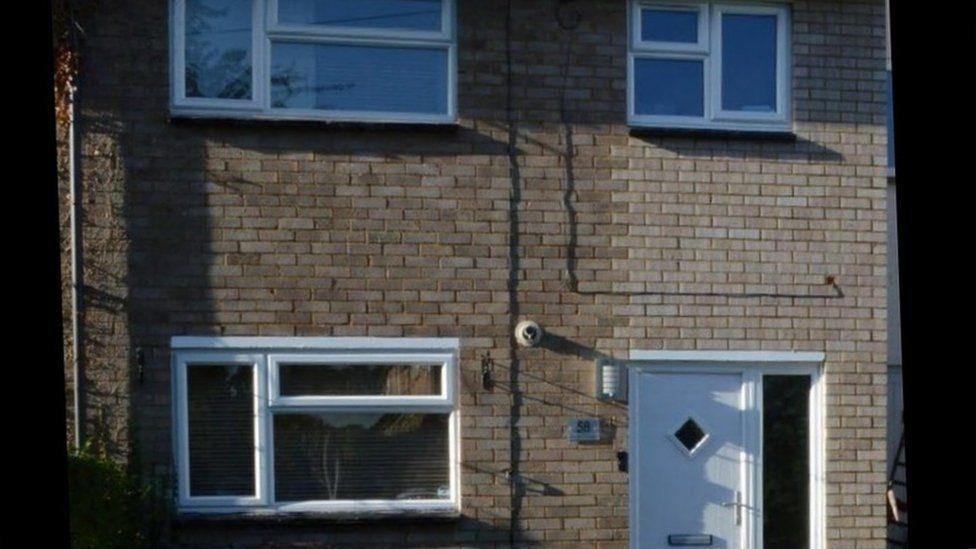 The outside of Carrick's former house. A small semi-detached property, two-storey brick property fitted with white plastic windows and a white front door.