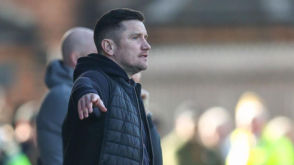 Crewe manager Lee Bell points out instructions to his players during a match